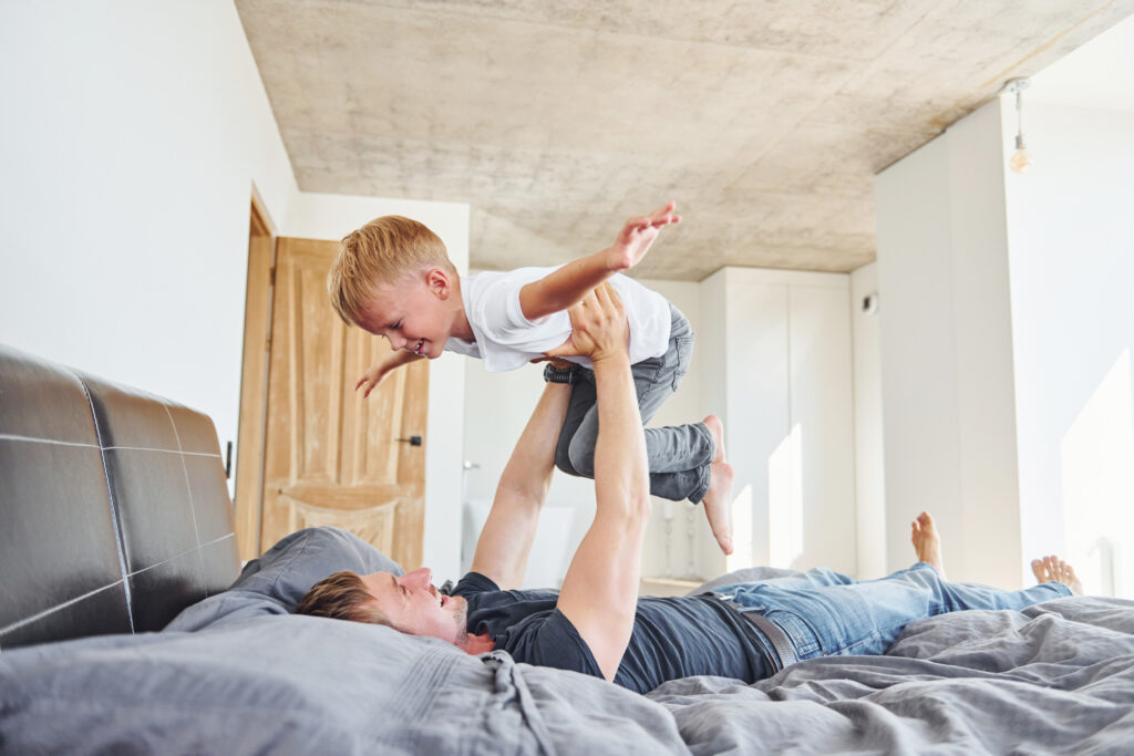 Laying down on the bed. Father and son is indoors at home together